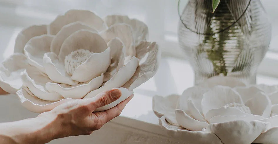 Hand holding a large white ceramic flower with another similar flower in the background by DABA Deco.
